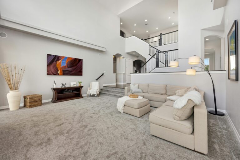Spacious modern living room featuring a beige sectional sofa, large flat-screen TV, and elegant staircase.